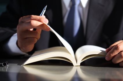 A person in suit and tie writing on an open book.